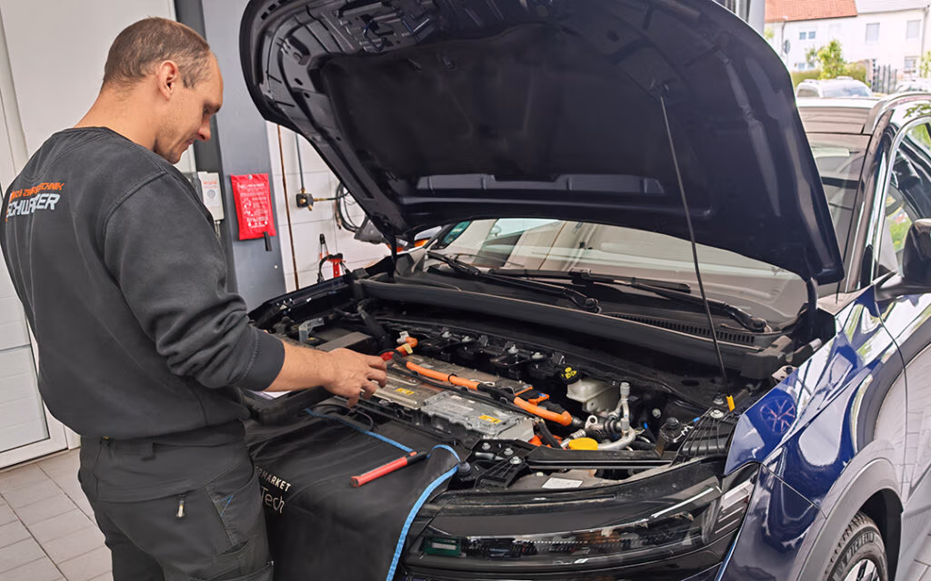 Mechaniker führt mit einem Gerät an einem E-Auto bei geöffneter Motorhaube eine Diagnose durch