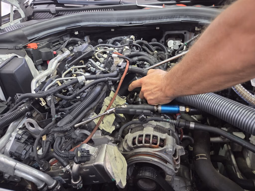 Mechaniker reinigt den Ansaugtrakt eines Motors mit einer Strahlpistole.
